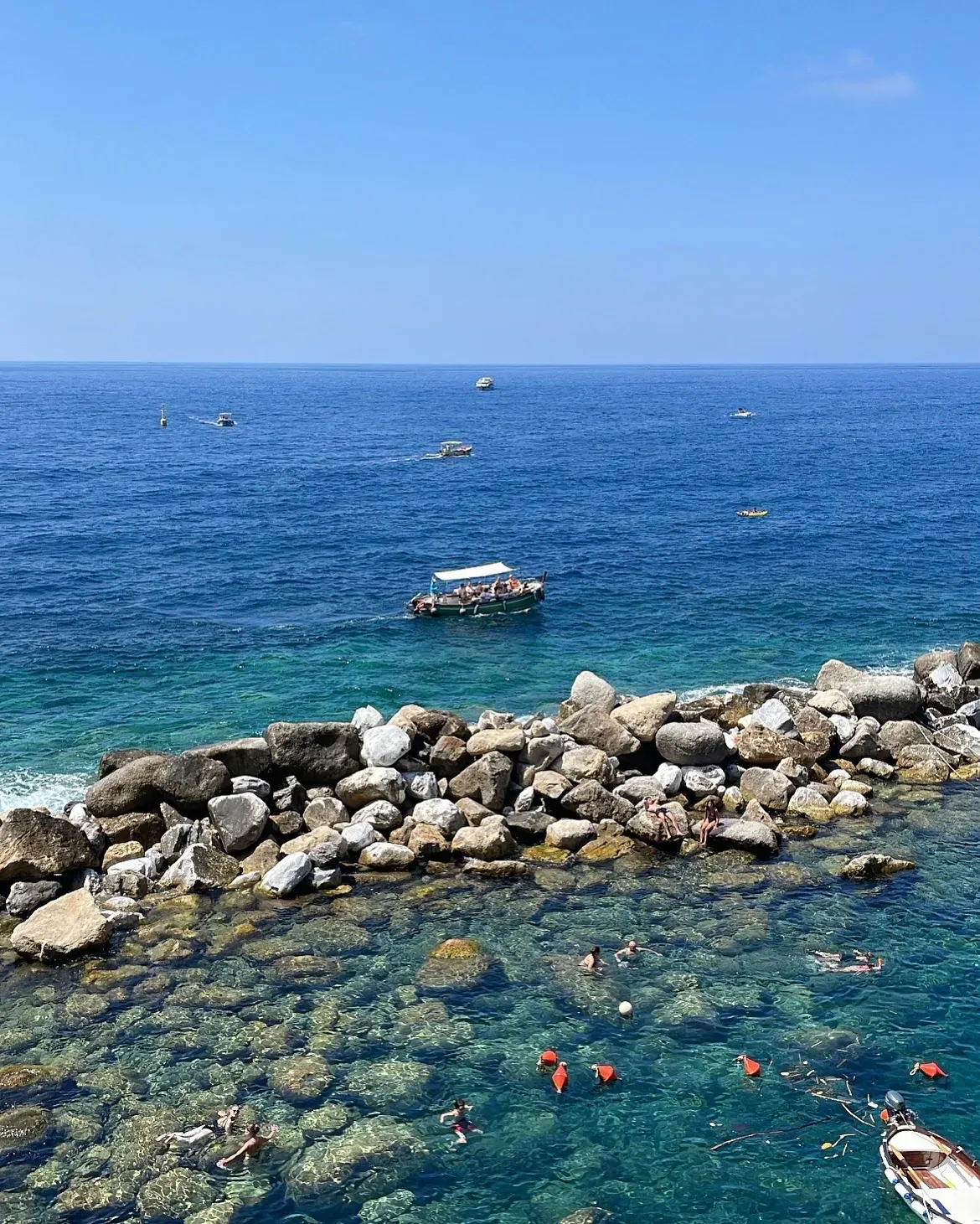 Small boats on blue water beyond a rocky swimming cove.